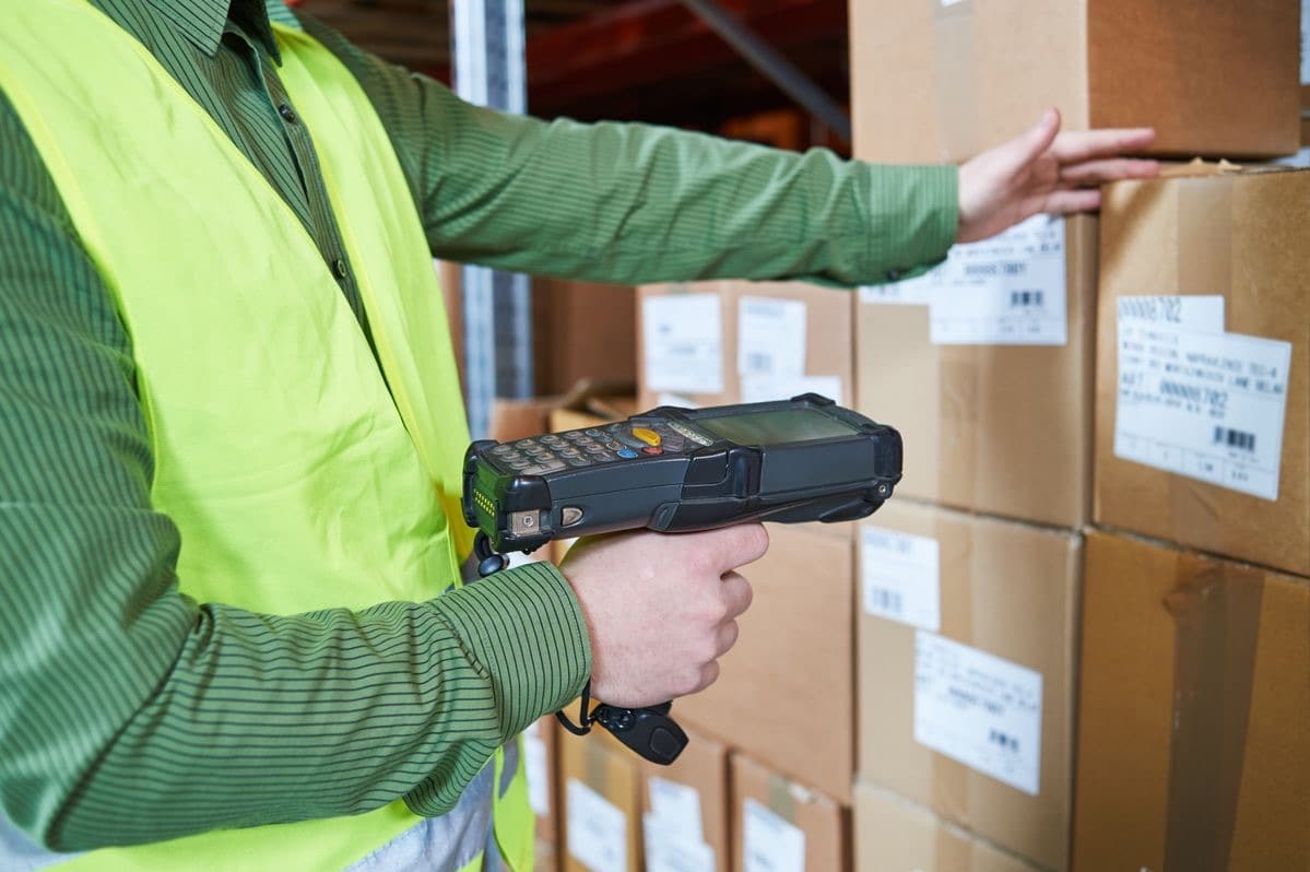 A gloved hand scanning RFID-tagged cartons on a warehouse shelf